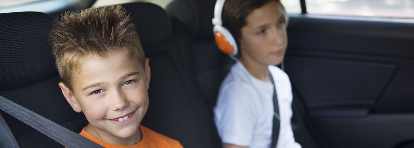 Two young boys sitting  in a car  playing tablet and smart phone